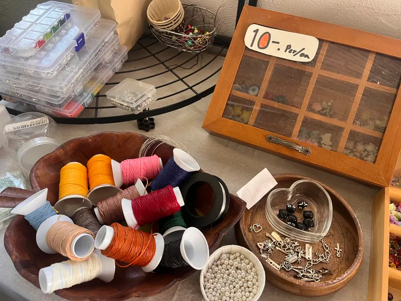 Colorful thread spools, beads, and charms in a wooden bowl at KIN-GYO workshop